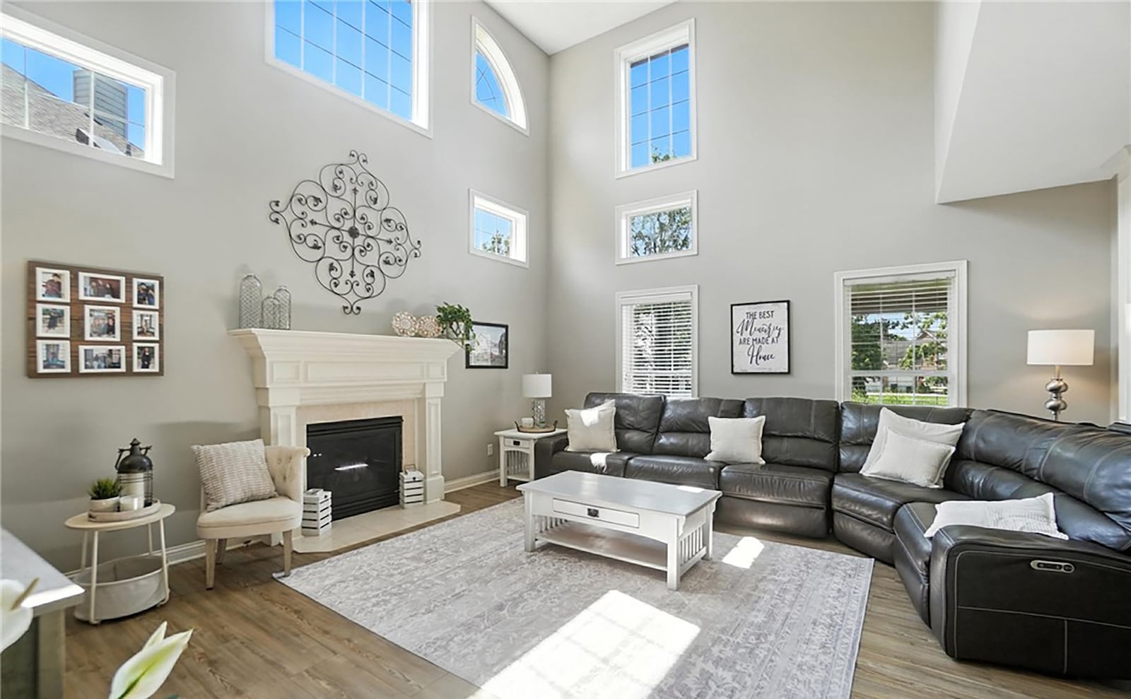 The two story great room has LVT flooring and windows near the top. There is a gas fireplace and a ceiling fan. CONTRIBUTED