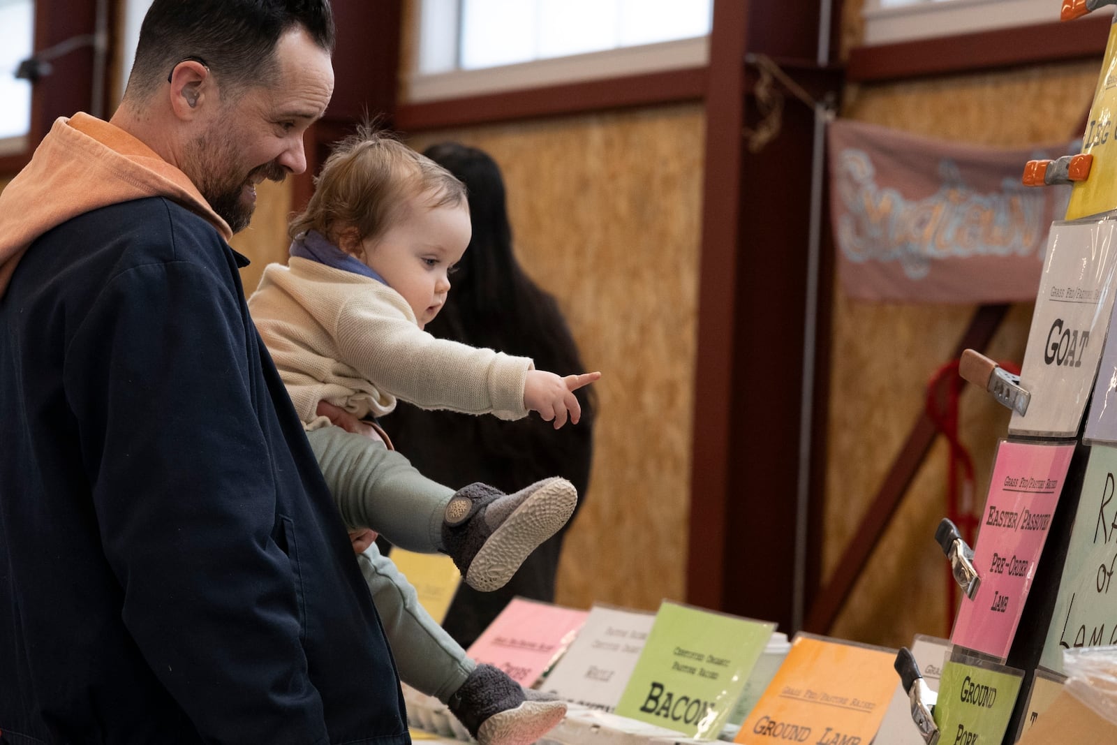 Aaron Swindle and his daughter Zoe look at product price signs at the Brighton Farmers Market on Sunday, March 23, 2025, in Brighton, N.Y. (Caitlyn Daproza via AP)