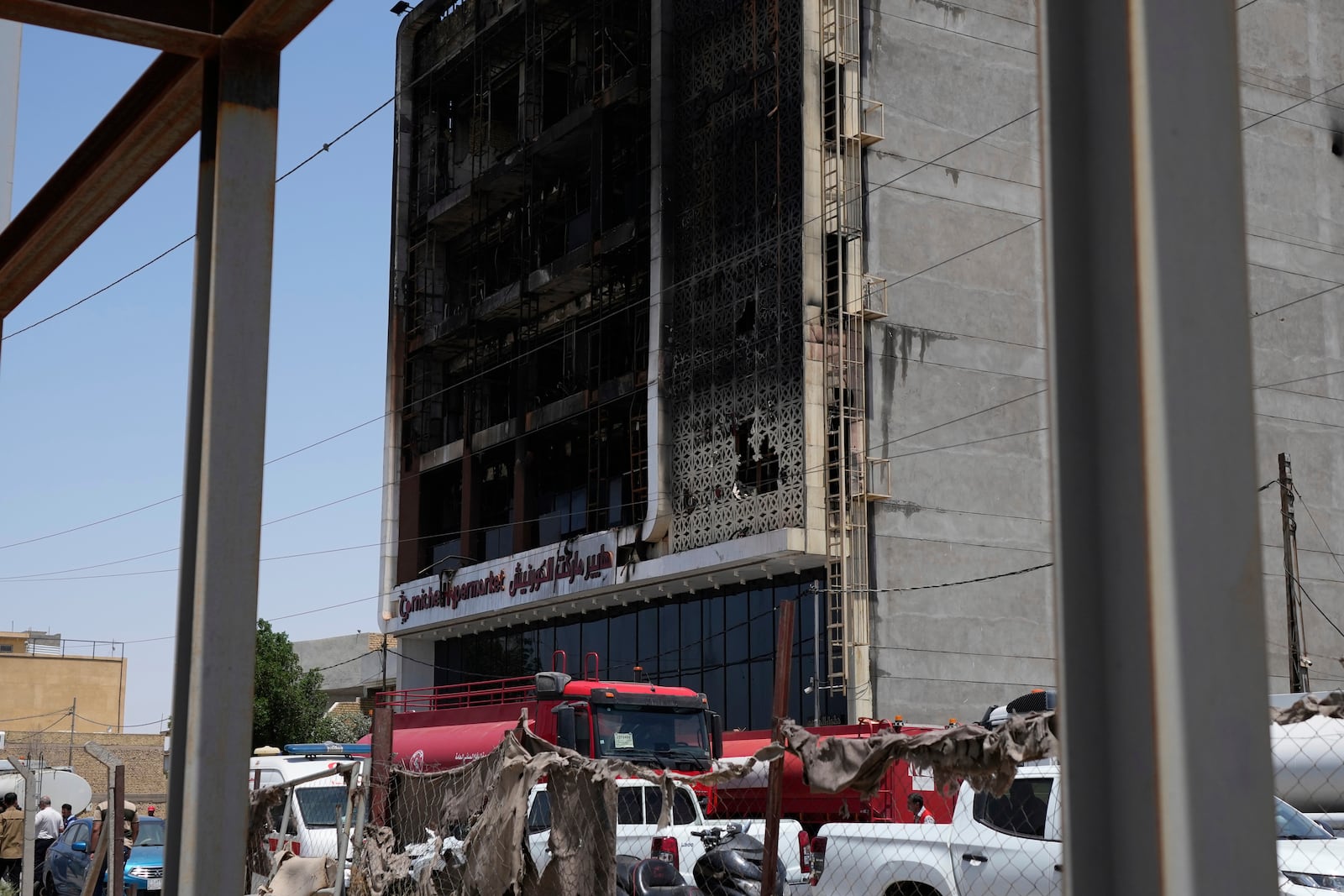 Firefighters gather in front of a burnt building in Kut, Iraq, Thursday, July 17, 2025 following a fire. (AP Photo/ Hadi Mizban)