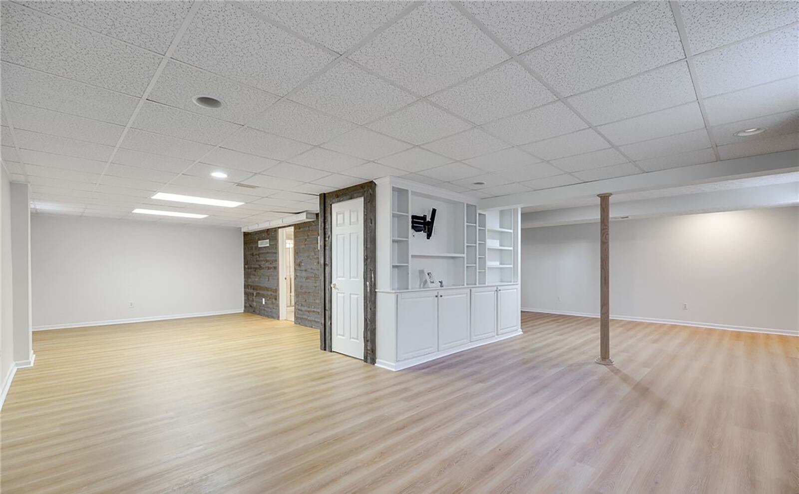 The basement recreation room has vinyl tile flooring, a built in entertainment center and a decorative wood paneled wall.
