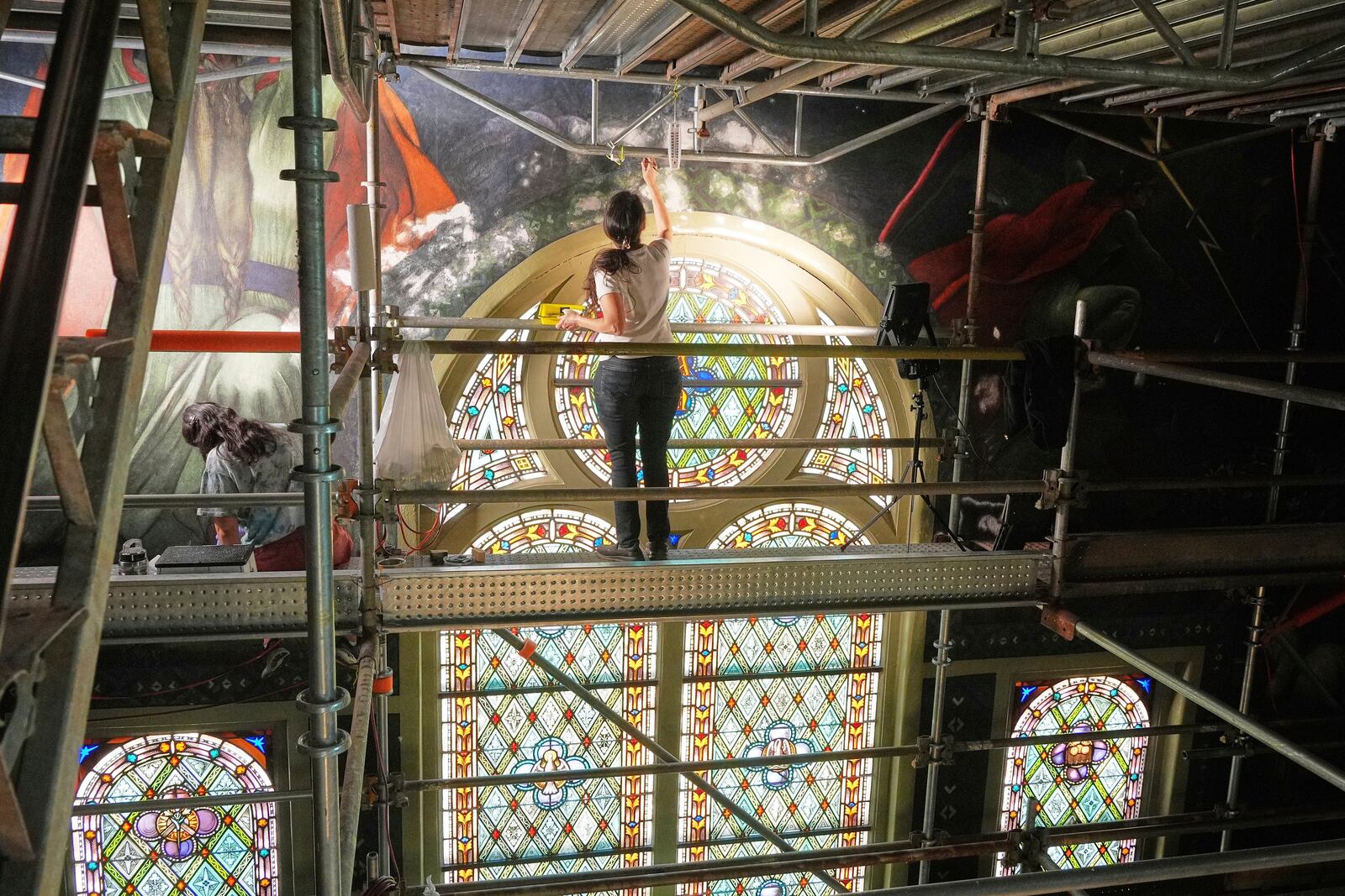 Standing on a 32-foot-tall scaffold, conservation technician Celeste Parrendo works on touching up a mural by Maxo Vanka inside St. Nicholas Croatian Catholic Church in Millvale, Pa., Monday, May 19, 2025. (AP Photo/Gene J. Puskar)
