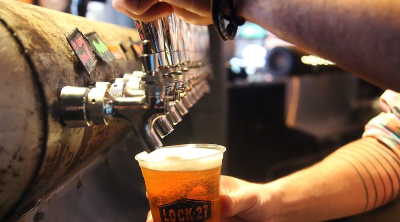 Louis Connelly, a bartender at Lock 27 Brewing in downtown Dayton, pours beer into a plastic cup used in response to the coronaviurs. The restaurant is also using disposable menus, has removed communal salt and pepper shakers and mustard and ketchup bottles from tables and offers plastic cutlery.  LISA POWELL / STAFF