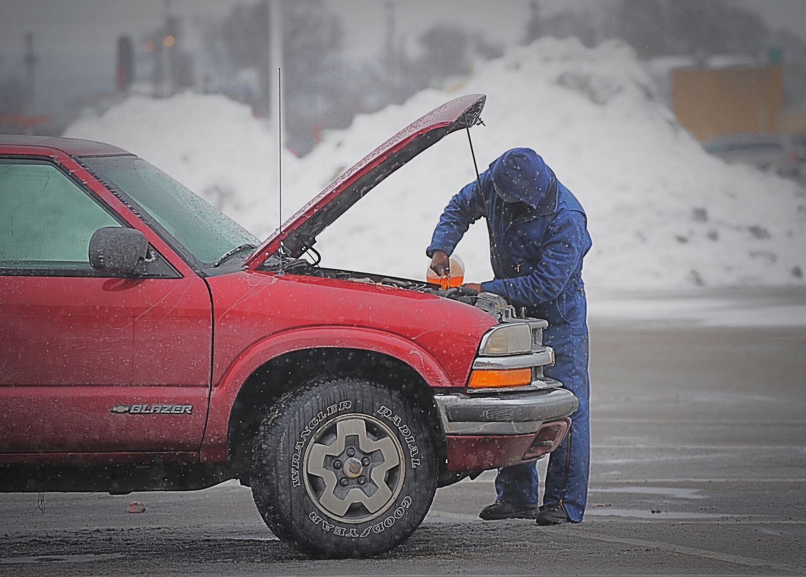 With piles of snow plowed up behind him a man puts windshield washing fluid in his vehicle at the Airway Shopping Center to be prepared for more winter weather Monday, February 15, 2021. MARSHALL GORBY/STAFF