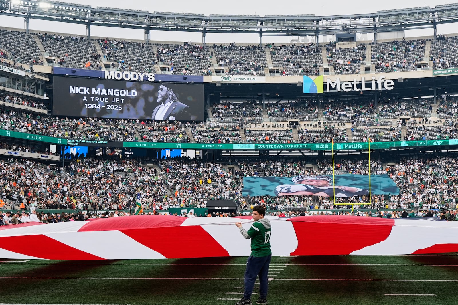 A large USA flag and a tribute to Nick Mangold, former Jets center who recently passed away, are on display before an NFL football game between the Cleveland Browns and the New York Jets, Sunday, Nov. 9, 2025, in East Rutherford, N.J. (AP Photo/Yuki Iwamura)