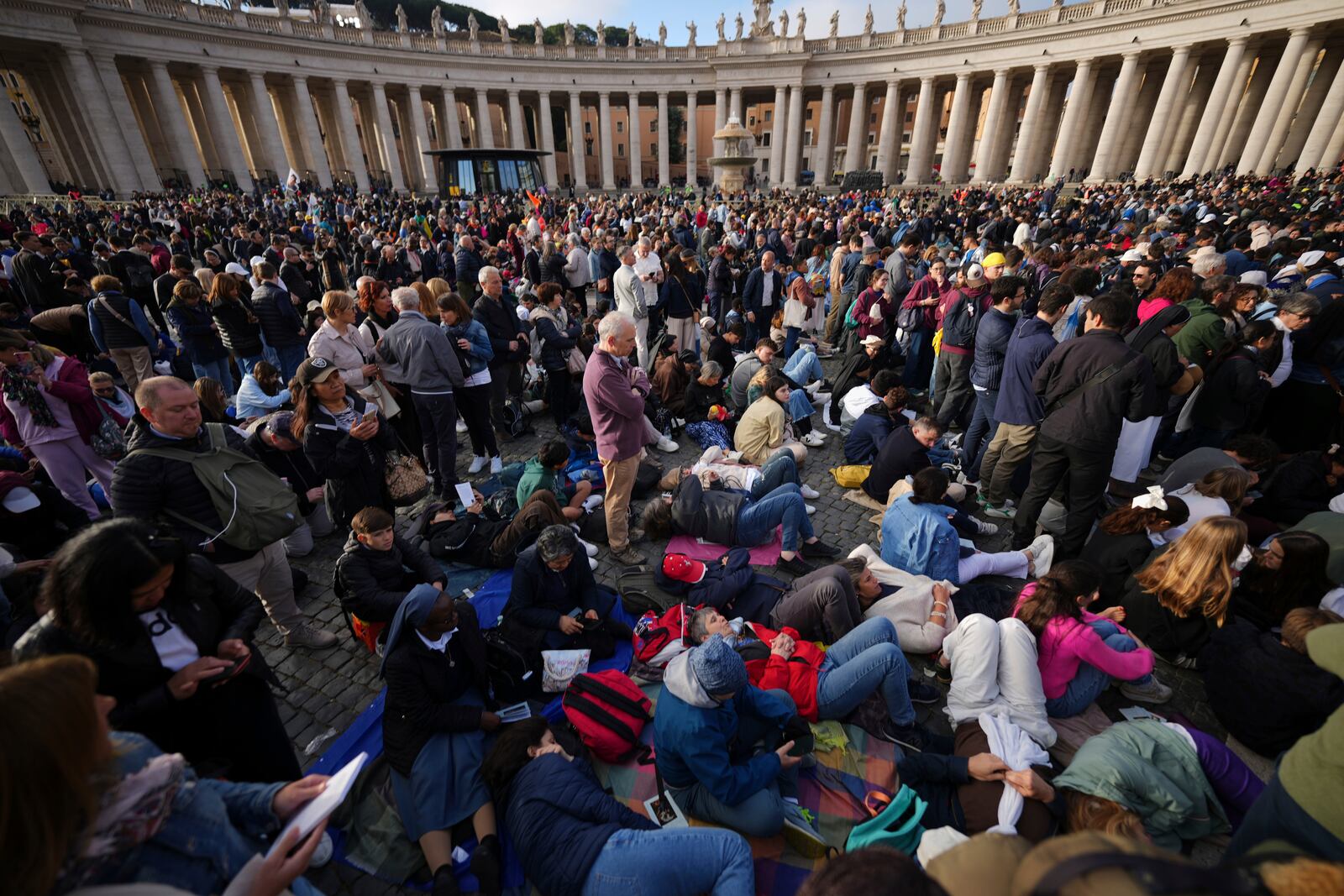 Faithful rest on the ground ahead of the funeral of Pope Francis in St. Peter's Square at the Vatican, Saturday, April 26, 2025. (AP Photo/Andrew Medichini)