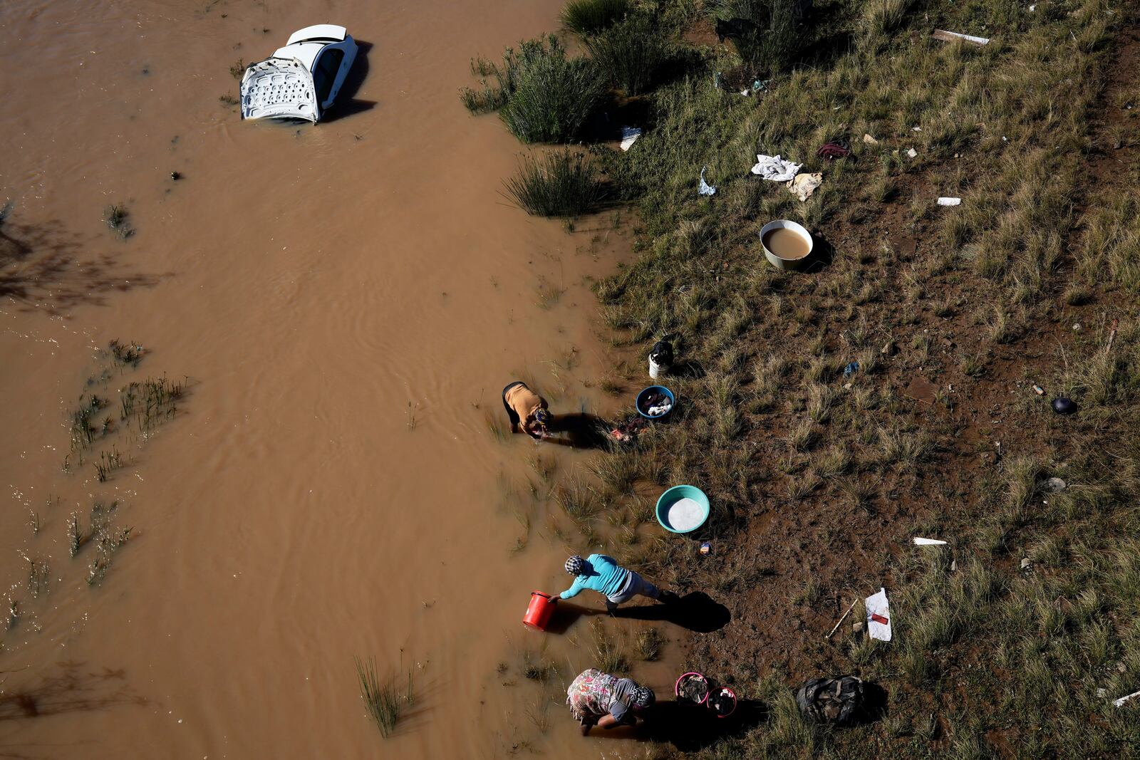 Women wash their clothes along the river next a car that was swept through by floods in Mthatha, South Africa, Thursday, June 12, 2025. (AP Photo/Themba Hadebe)