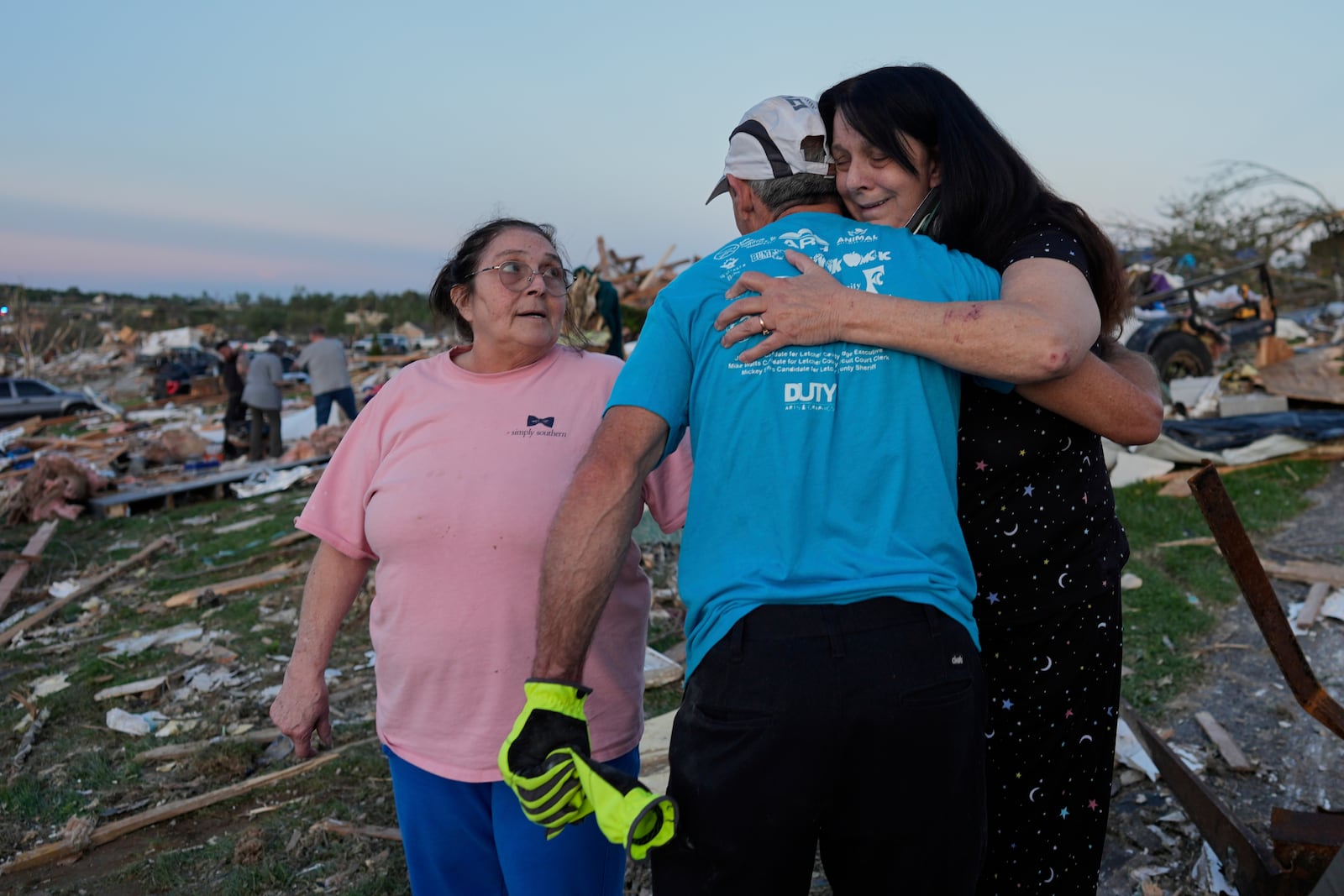 Bea Johnson, left, looks to her sister Kristie Sexton, right, as she is embraced by family friend Keith Adams as they stand next to Sexton's destroyed home after a severe storm passed through the area, Saturday, May 17, 2025, in London, Ky. (AP Photo/Carolyn Kaster)