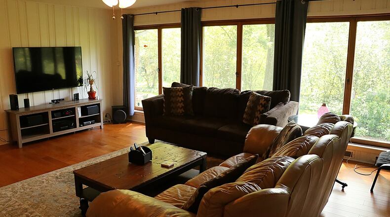 A wall of windows fills the family room with natural light and provides panoramic views of the tree-lined back yard. Pine paneling has been painted white to brighten the space, which also has a wood floor.