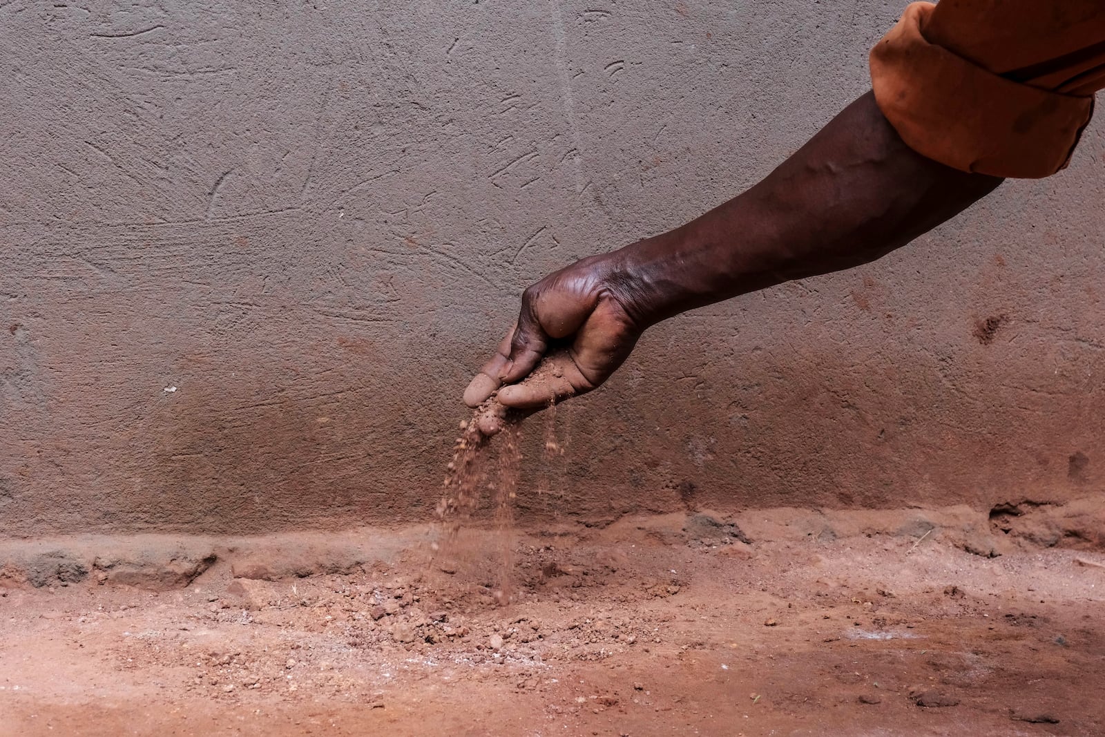 Simon Tigawalana shows dirt, that used to make up his home’s floor, before getting a clay-based earthen floor by a company called EarthEnable on May 16, 2025, in Jinja, Uganda. (AP Photo/Hajarah Nalwadda)