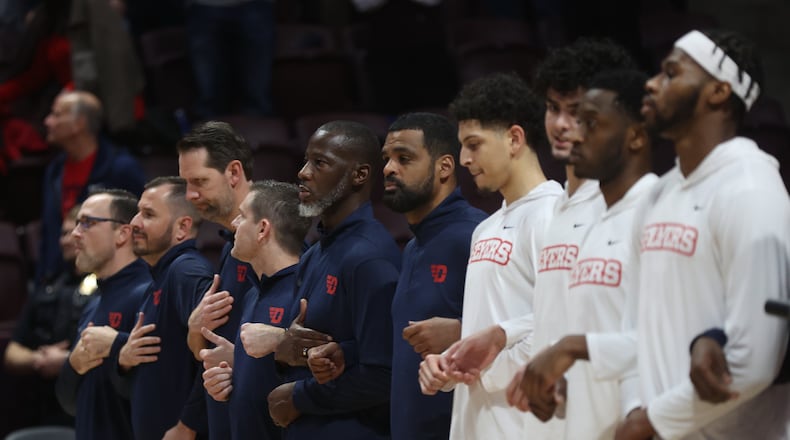 Dayton coaches, including Anthony Grant, and players stand for the national anthem before a game against Virginia Tech on Wednesday, Dec. 7, 2022, at Cassell Coliseum in Blacksburg, Va. David Jablonski/Staff