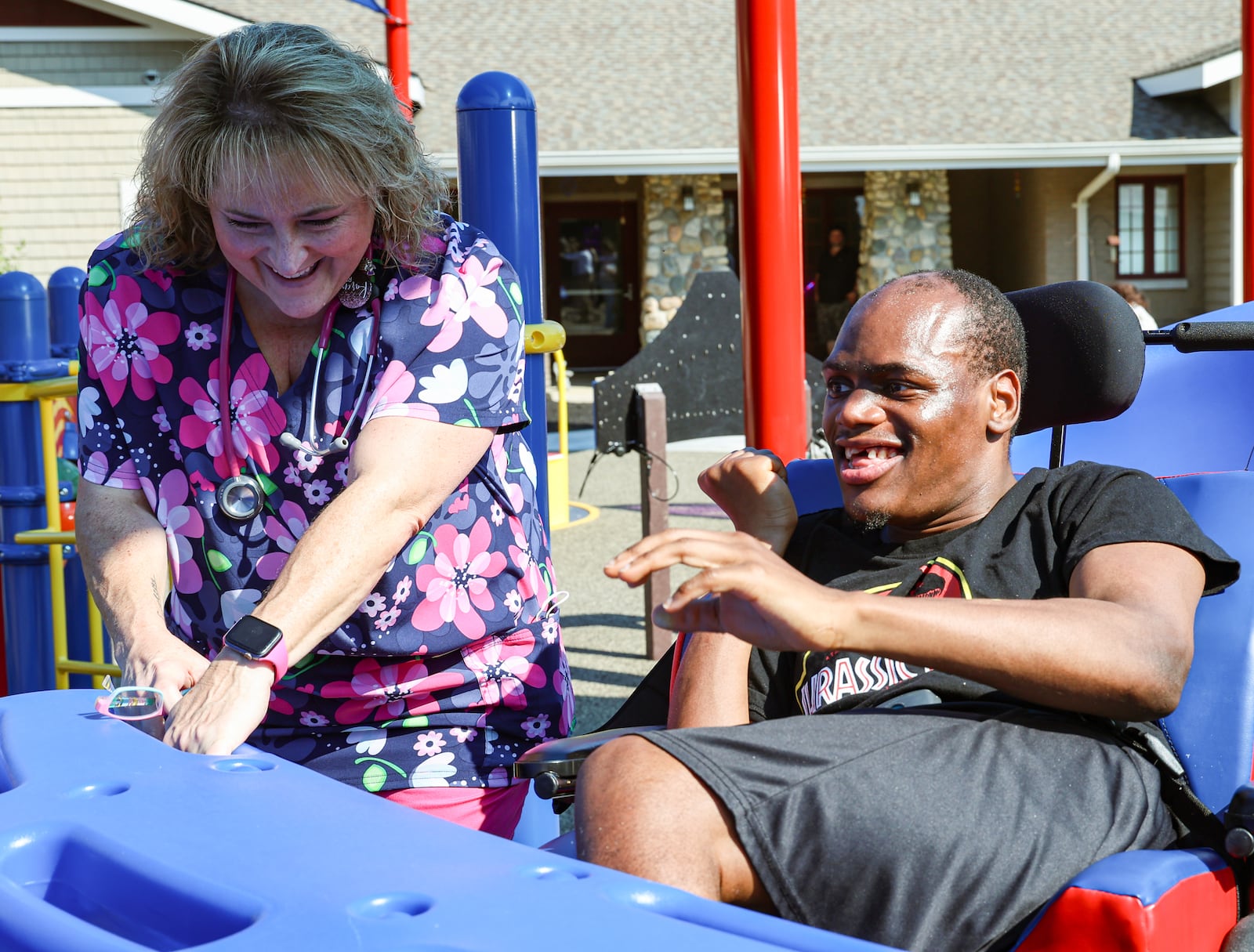 Karen McKeand, a nurse at Stillwater Center, helps rock Jason W., a patient at the center, on Friday, Aug. 8, during a dedication event for the center's playground, named The Cove. The playground is designed to be an inclusive and accessible space for Stillwater Center residents of all ages and abilities. BRYANT BILLING / STAFF