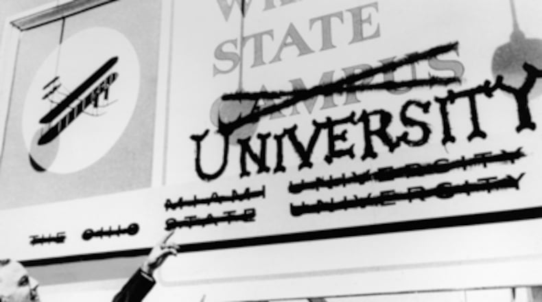 Wright State’s first president, Brage Golding, points at a sign with Miami University and Ohio State University crossed off at the bottom.