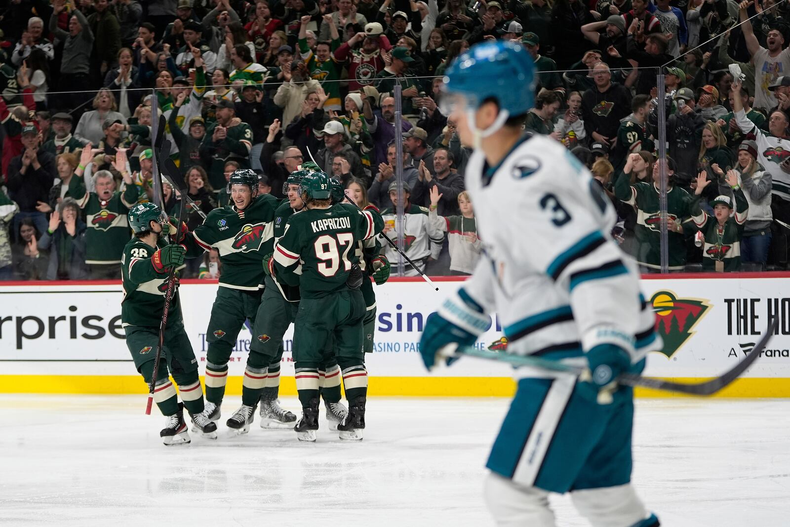 Minnesota Wild center Joel Eriksson Ek (14), middle, celebrates with teammates after scoring a goal as San Jose Sharks defenseman Henry Thrun (3), foreground, skates across the ice during the third period of an NHL hockey game, Wednesday, April 9, 2025, in St. Paul, Minn. (AP Photo/Abbie Parr)