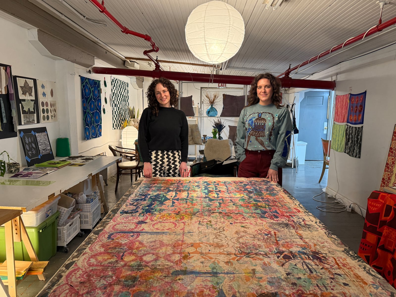 Textile artists Jess LaCava and Jane Tuss share one side of the studio. Here they stand together at Tuss' mother's old work table, covered in decades worth of screenprinting stencils. HANNAH KASPER/CONTRIBUTED