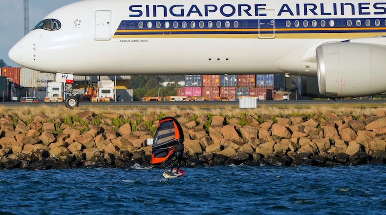 FILE - A man wing foils on Botany Bay as a Singapore Airlines passenger jet taxis after landing at Sydney Airport in Australia, Sept. 5, 2022. (AP Photo/Mark Baker, File)