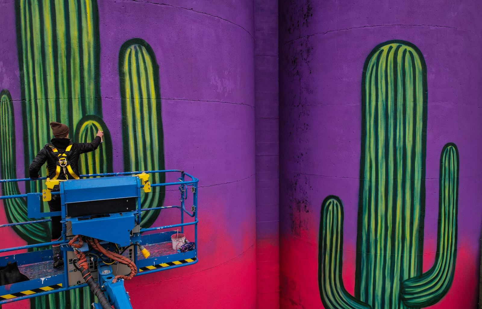 Centerville-raised muralist Erica Arndts paints a desert scene on the silos near 2nd Street Market. JIM NOELKER/STAFF
