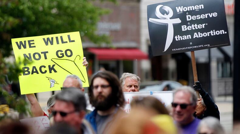 A pro-choice rally drew about 100 people to North Main Street in Dayton earlier this year. The group encouraged Premier Health to make a transfer agreement with Women’s Med Center, a move needed to keep the center open under to Ohio law. At right is an anti-abortion sign seen at the rally. TY GREENLEES / STAFF