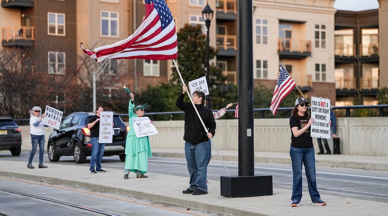 Protesters hold signs and flags amidst the arrival of federal law enforcement, Tuesday, Nov. 18, 2025, in Charlotte, N.C. (AP Photo/Matt Kelley)