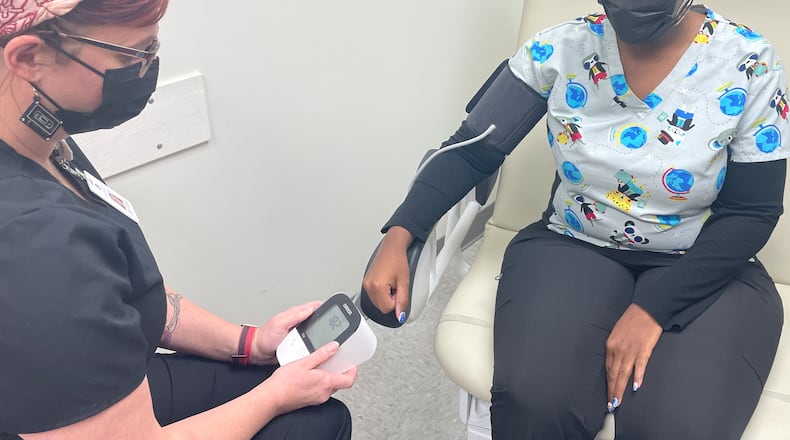 Angie Holycross, RN care coordinator with the Community Health Centers of Greater Dayton (left), along with nurse Dalisa Turner (right) demonstrate how to use the blood pressure monitor patients utilize in the health centers’ current program being funding by the National Hypertension Control Initiative Grant. SAMANTHA WILDOW\STAFF