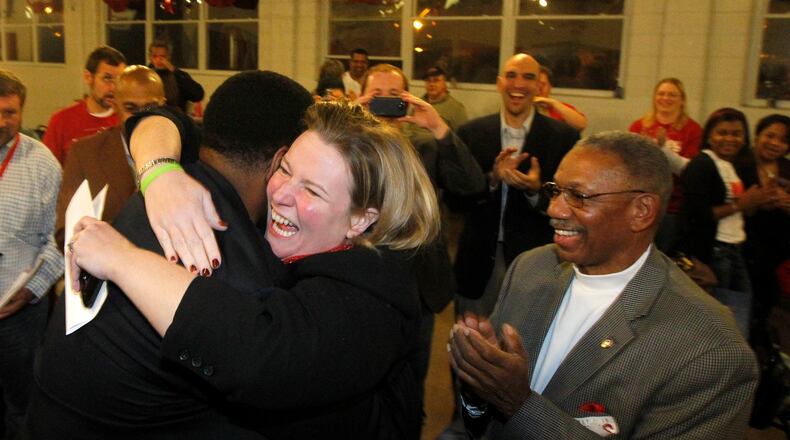 Mayor elect Nan Whaley is hugged by Dayton city commissioner Joey Williams while Jeff Mims (right) applauds Tuesday night at Democratic headquarters in Dayton. Both Williams and Mims won a seat on the city commission. LISA POWELL / STAFF