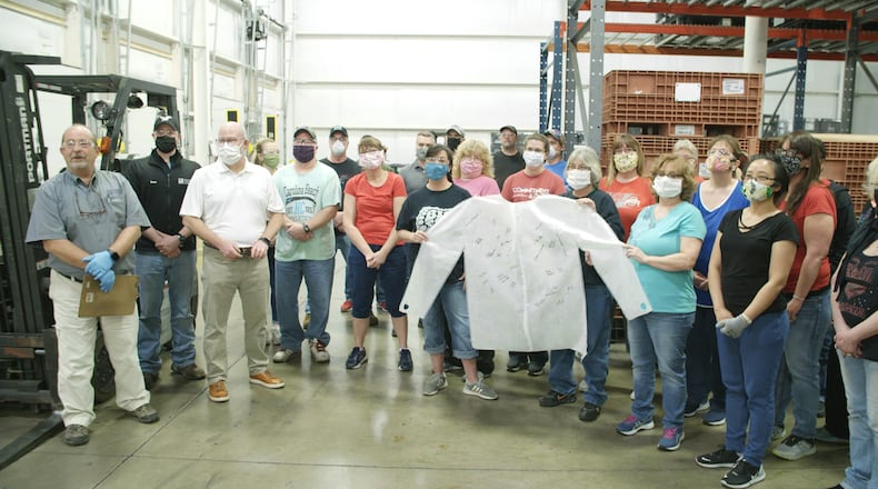 Employees at IPC in Piqua stand with a gown produced for medical staff at Miami Valley Hospital.