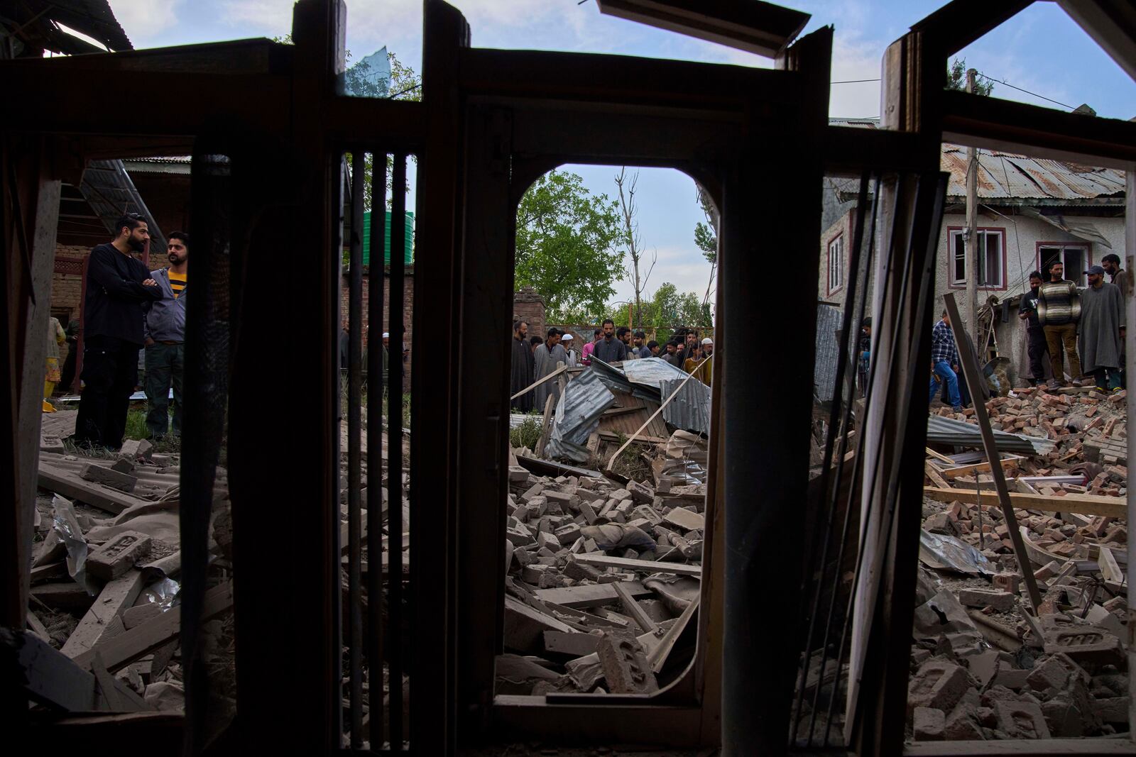 Kashmiri villagers inspect the debris of the blown-up family home of Ahsan Ul Haq Shiekh, a militant who officials say is involved in the deadly attack on tourists in Pahalgam, seen through the window of partially damaged house of a neighbor at Murran village in Pulwama, south of Srinagar, Indian controlled Kashmir, Saturday, April 26, 2025. (AP Photo/Dar Yasin)