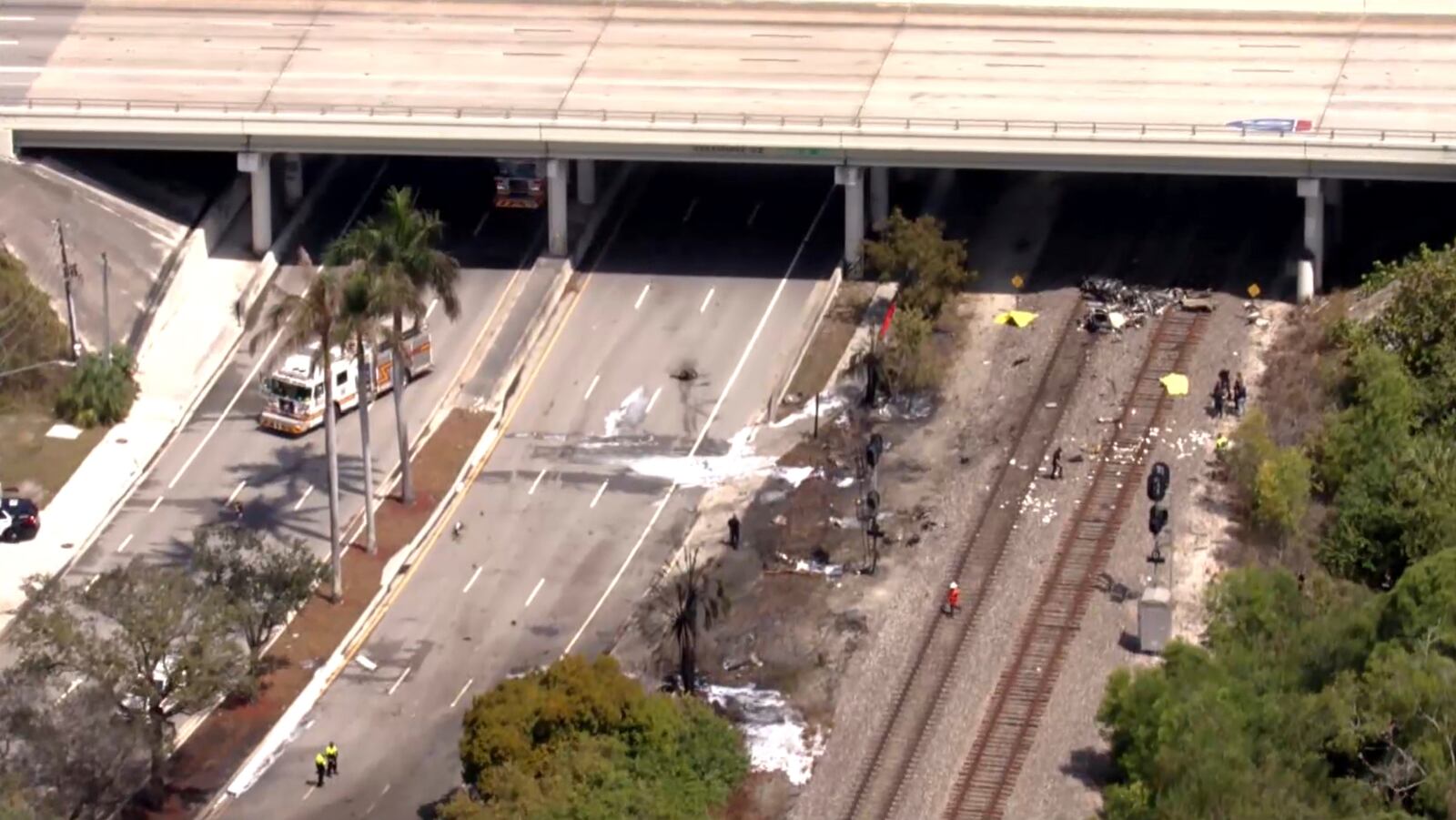 In this image taken from video provided by WSVN-TV, emergency personnel respond to the area where a small plane crashed on the railroad tracks beneath the overpass near Interstate 95 in Boca Raton, Fla., Friday, April 11, 2025. (WSVN-TV via AP)
