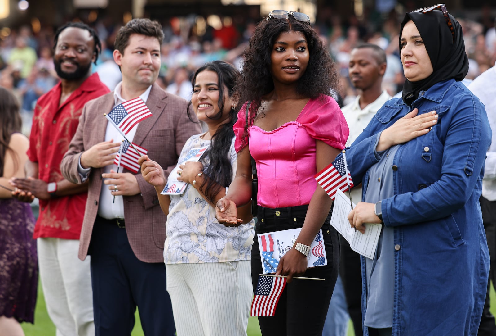 Twenty immigrants became U.S. citizens during a naturalization ceremony on Tuesday, Aug. 5, between the third and fourth innings during a Dayton Dragons game at Day Air Ballpark, including Aziza Yenga (center right, in pink) who immigrated from Tanzania. BRYANT BILLING / STAFF