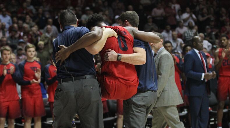 Dayton trainers Mike Mulcahey and Patrick O’Neal carry Josh Cunningham off the court after he was injured in the final seconds against Alabama on Tuesday, Nov. 15, 2016, at Coleman Coliseum in Tuscaloosa, Ala. David Jablonski/Staff
