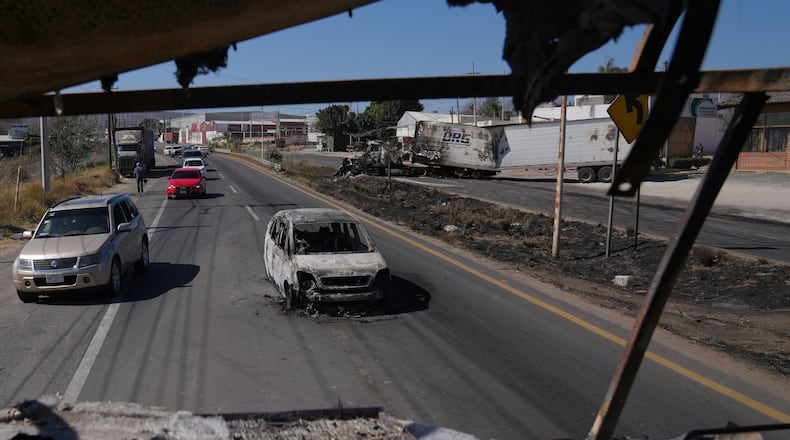 Vehicles pass a burned car a day after the Mexican army killed the leader of the Jalisco New Generation Cartel, Nemesio Oseguera Cervantes, known as "El Mencho," in Guadalajara, Mexico, Monday, Feb. 23, 2026. (AP Photo/Marco Ugarte)