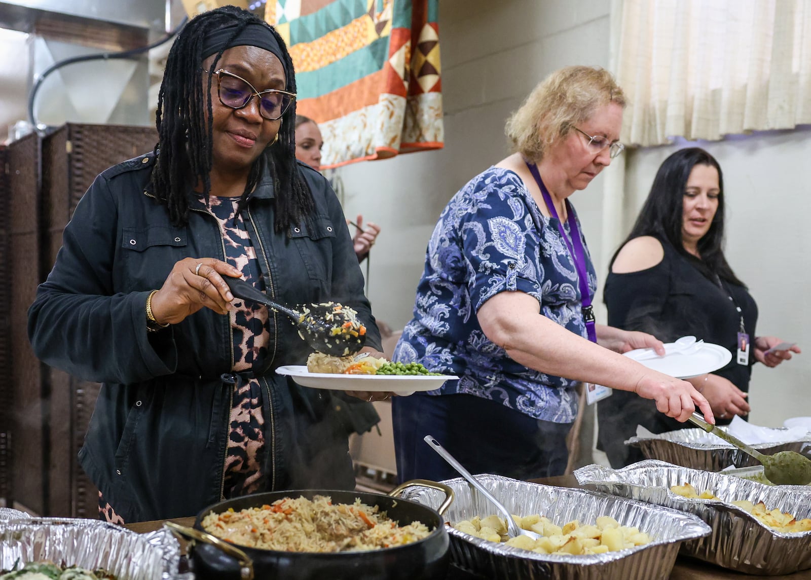 Dr. Chi Adeliyi (left), the director of East Dayton Fellowship Community Development Initiatives, scoops food on her plate during a lunch hosted by Cross Over Community Development on May 13 at Christ Evangelical Lutheran Church. BRYANT BILLING / STAFF