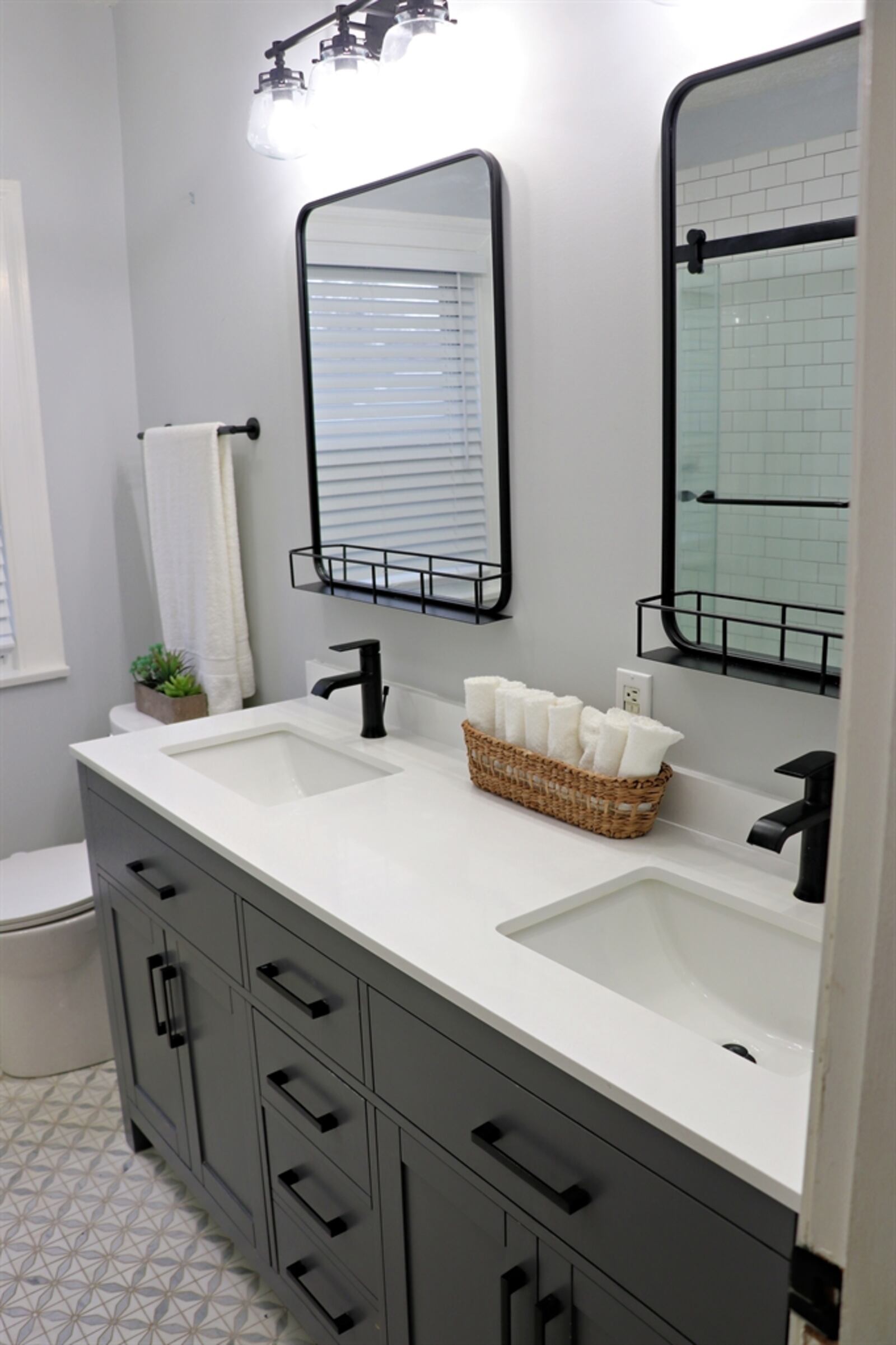 This bathroom has a whirlpool tub-shower with glass doors and a double-sink elevated vanity with updated mirrors and light fixtures.