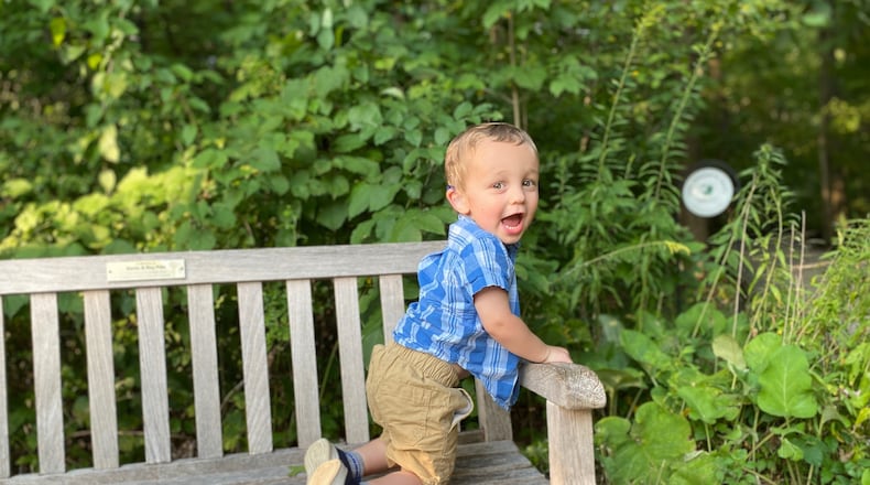 Thomas Harris, two years old, climbs on a park bench looking back excitedly at the camera.