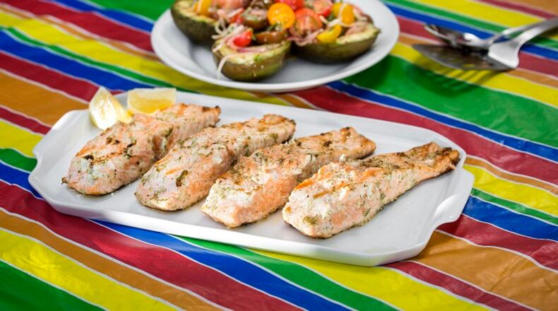 Grilled salmon on the table. The salmon were brushed with dill mayonnaise, accompanied by grilled avocado halves brushed with mayonnaise, salt and pepper, then topped with marinated tomato salad. (Ricardo DeAratanha/Los Angeles Times/TNS)