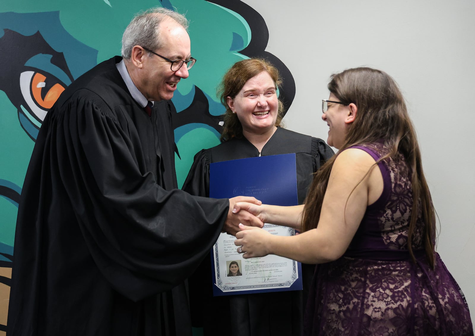 U.S. District Court Judge Michael Newman (left) and U.S. Magistrate Judge Caroline Gentry (center) greet Despina Lawandi-Riegel shortly after she received her certificate of naturalization following a ceremony between the third and fourth innings at a Dayton Dragons game on Tuesday, Aug. 5 at Day-Air Ballpark. She was one of 20 immigrants to participate in a naturalization ceremony on Tuesday. BRYANT BILLING / STAFF