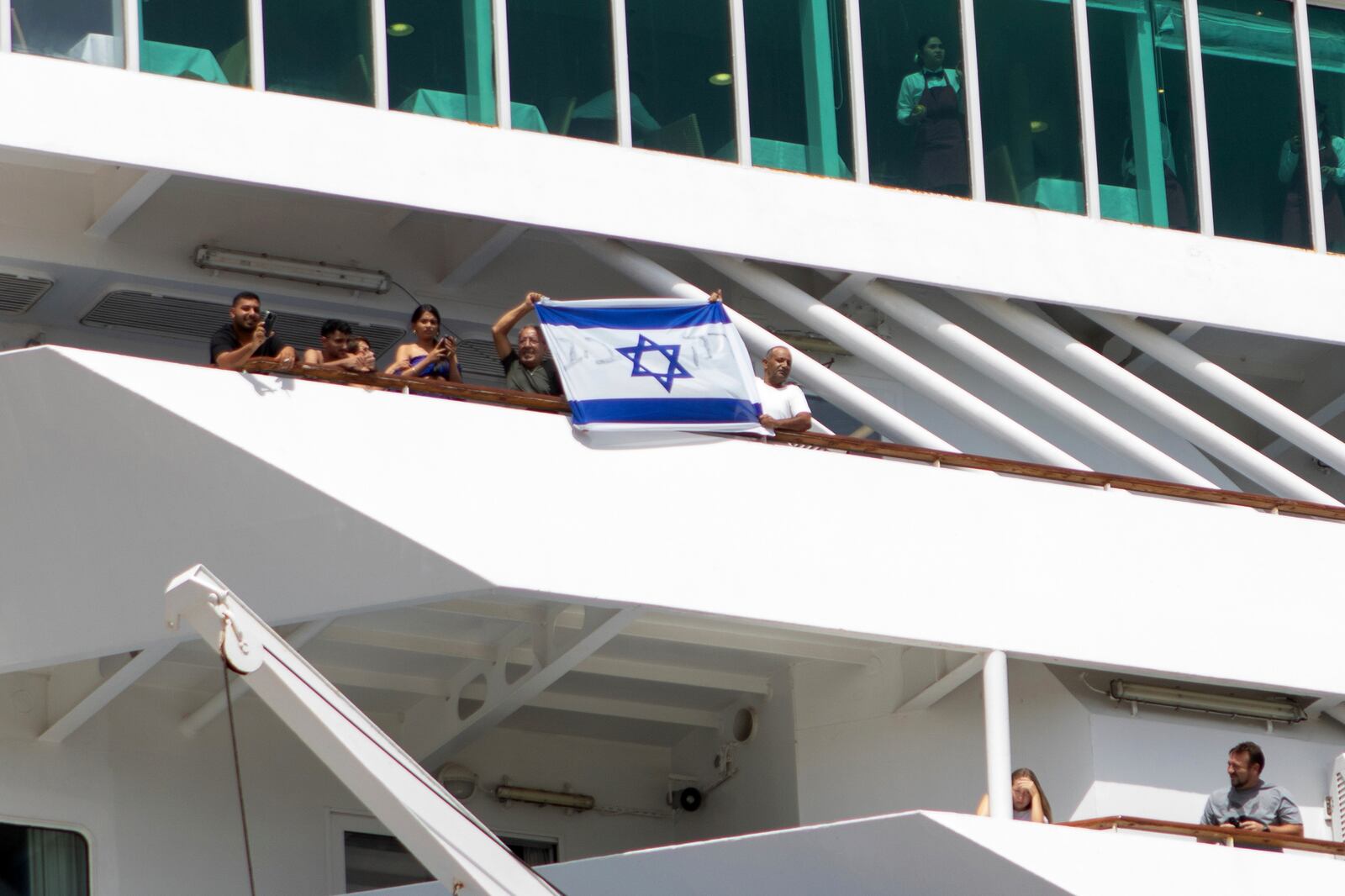 Two men hold up an Israeli flag during the departure of a cruise ship carrying Israeli tourists on the southeastern Aegean Sea island of Rhodes, Greece, Monday, July 28, 2025. (InTime News via AP)