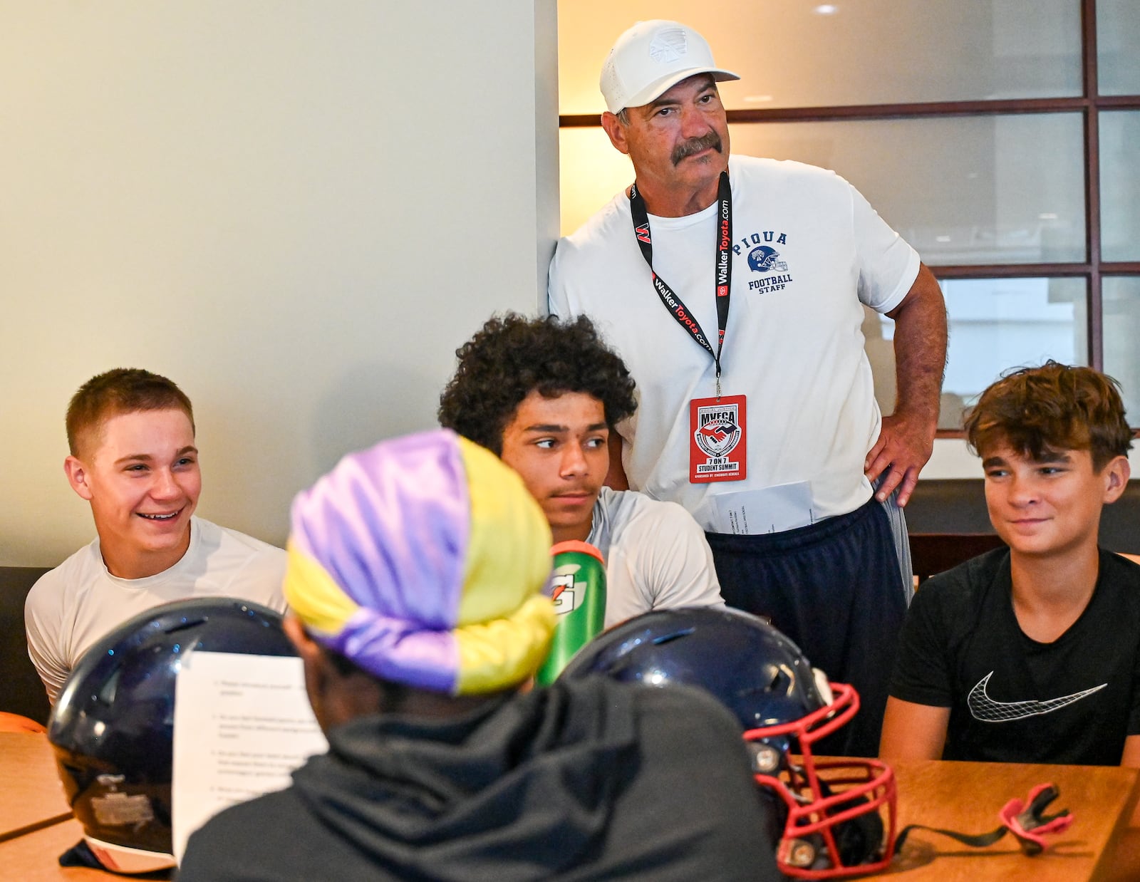 Players from Northmont, Piqua, Alter and Middletown talk under the watch of longtime Piqua coach Bill Nees during a meet and greet session at University of Dayton Arena during the Miami Valley Football Coaches Association's Social Justice 7-on-7 on Wednesday, July 9. BRYANT BILLING / STAFF