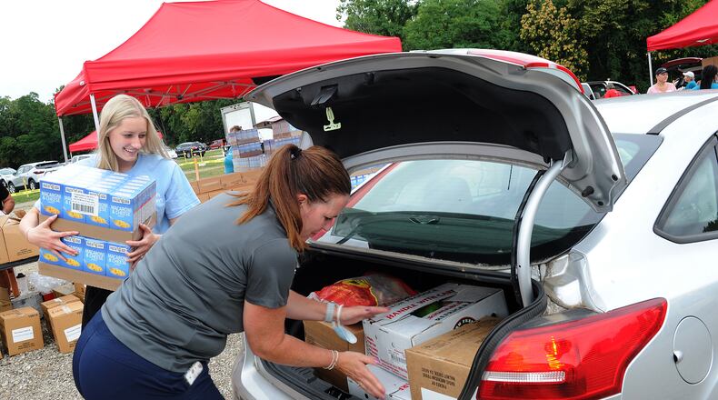 Ashtyn Grabtree, left, and Bridgett Hobbs loads food into the trunk of a car Tuesday Aug. 16, 2021, during the mass drive-thur food distribution at the Dixie Twin Drive-In hosted by the Foodbank. MARSHALL GORBY\STAFF