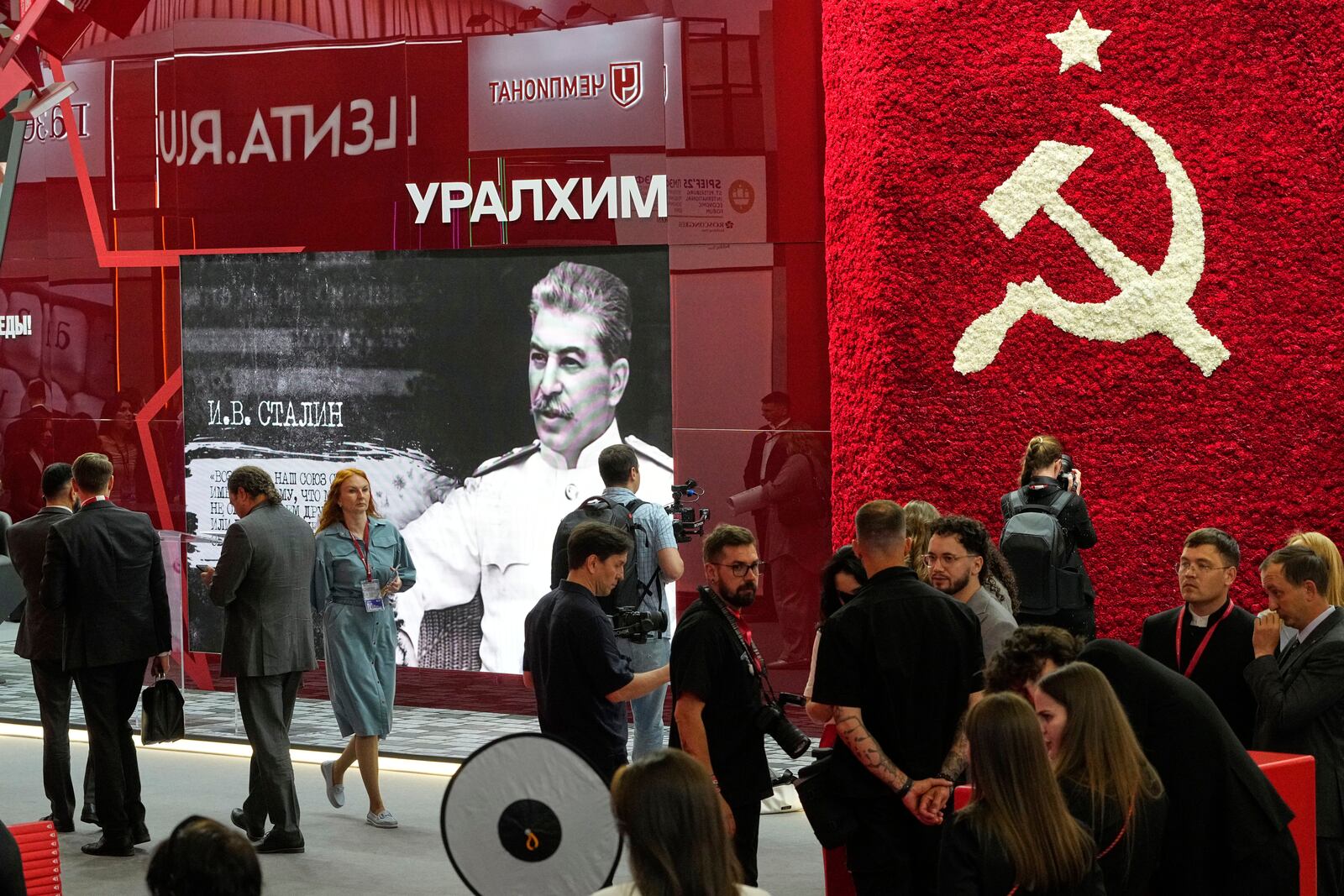 Guests and participants walk in front of an image of Soviet Leader Josef Stalin and a Soviet symbol on the sidelines of the St. Petersburg International Economic Forum in St. Petersburg, Russia, Wednesday, June 18, 2025. (AP Photo/Dmitri Lovetsky)