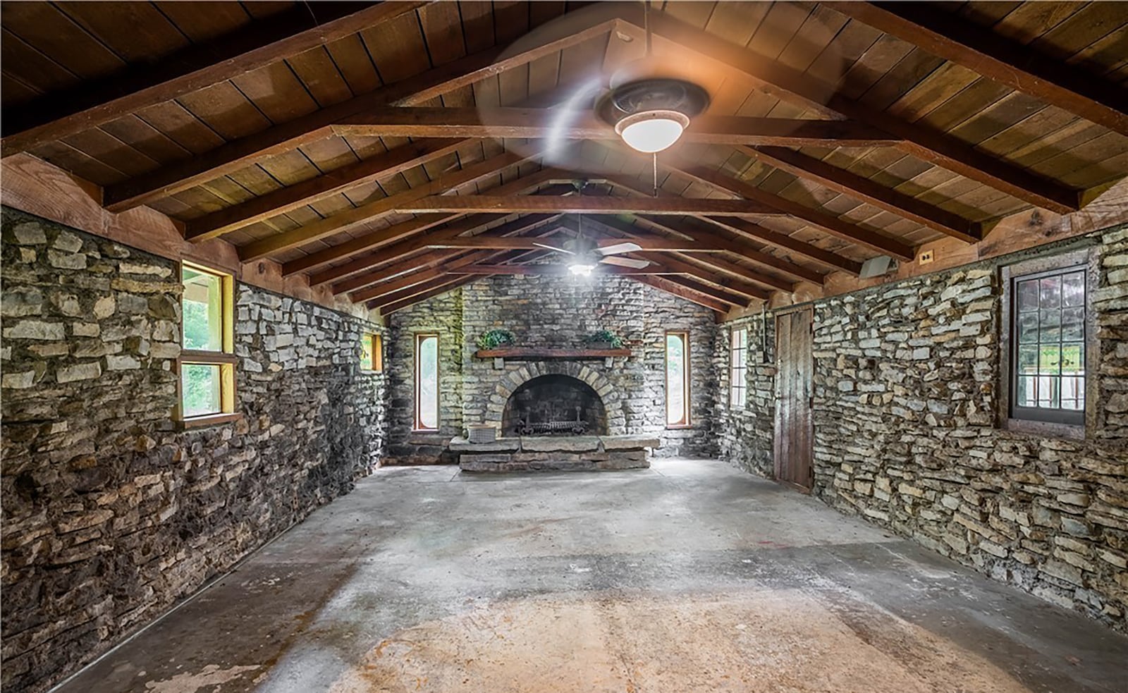 The living room features original stone walls and a woodburning fireplace. It also has beamed wood ceilings