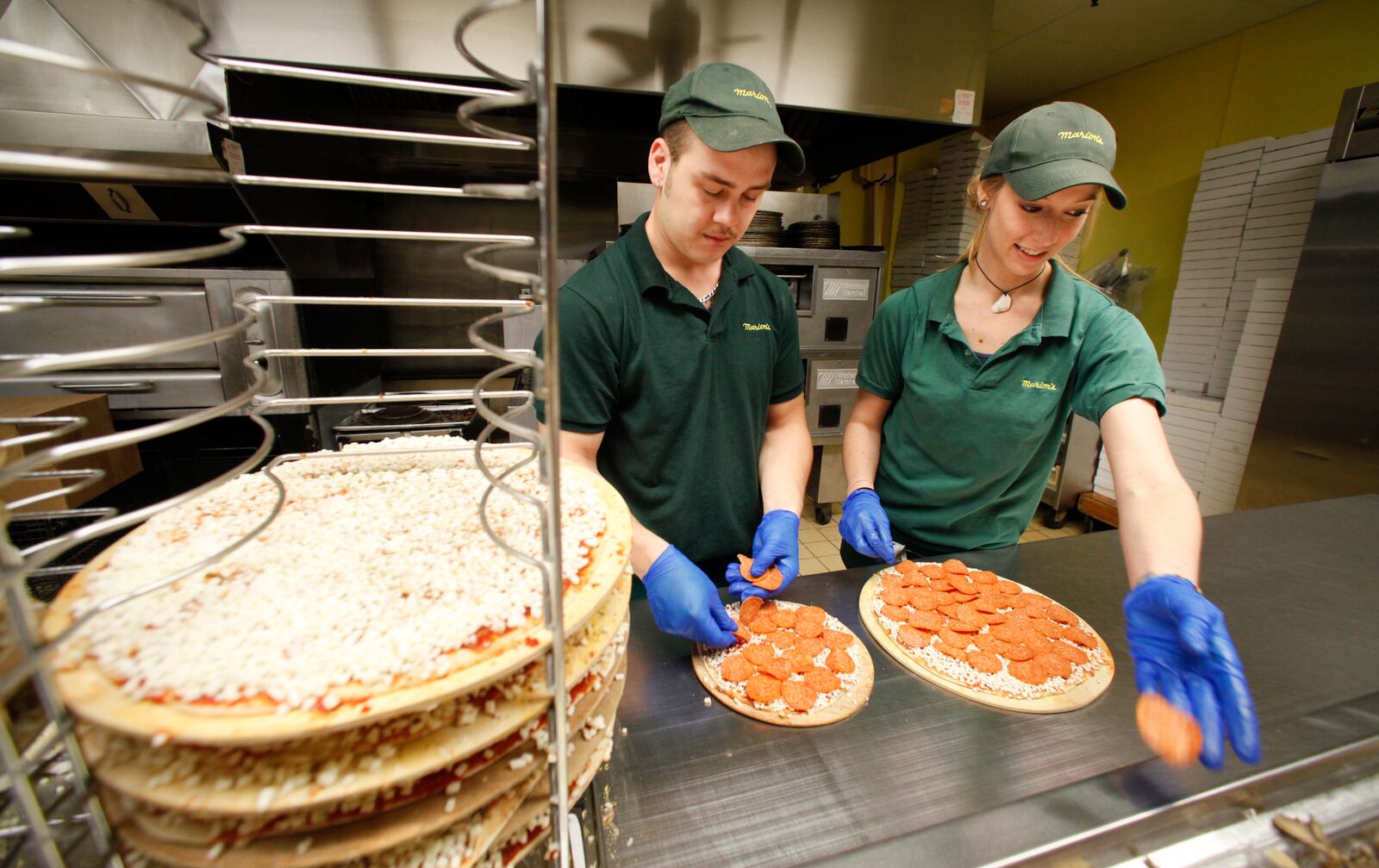 Marion's Pizza employees Robert Bechtolt IV and Tiffany Book add ingredients to a pie on Wednesday, December 12, at the Shroyer at Patterson Road location. Expansion into Mason was a factor the Dayton-based company cited for beginning to accept credit cards. CHRIS STEWART / STAFF