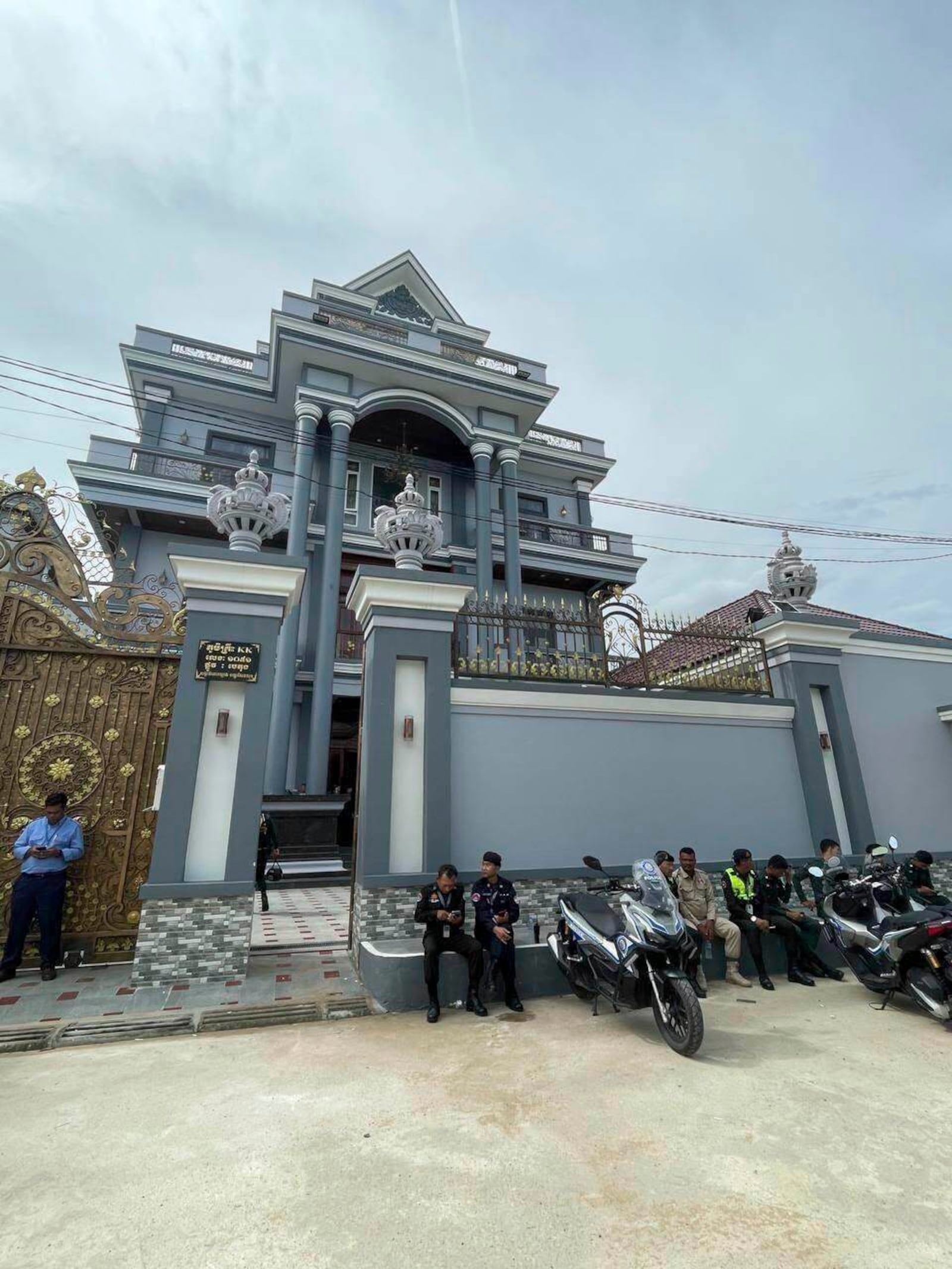 In this photo provided by state news service Agence Kampuchea Press, police stand in front a villa that served as an alleged cyberscam center on the outskirts of the capital Phnom Penh, Cambodia, which was raided on Friday, July 18, 2025. (AKP via AP)