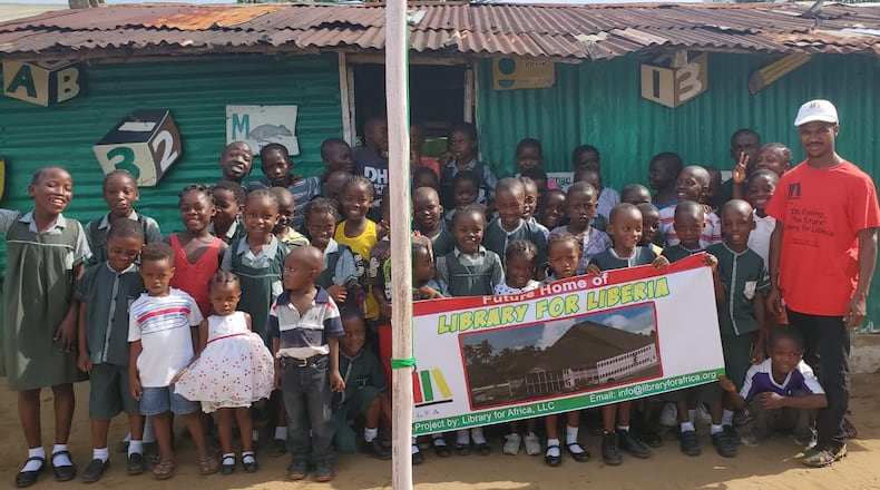 Co-Founder of Library for Africa, Darius Ricks, with students from Ardju Preparatory and Daycare Center holding a banner o the future Library of Liberia.