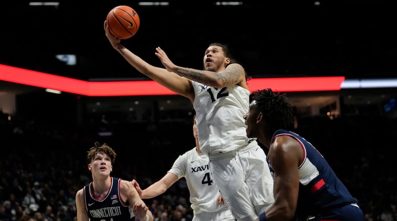 Xavier forward Tre Carroll (12) drives to the basket as UConn guard Braylon Mullins (24), Xavier forward Filip Borovicanin (4), and UConn forward Tarris Reed Jr. (5) took on during the first half of an NCAA college basketball game, Wednesday, Dec. 31, 2025, in Cincinnati. (AP Photo/Carolyn Kaster)