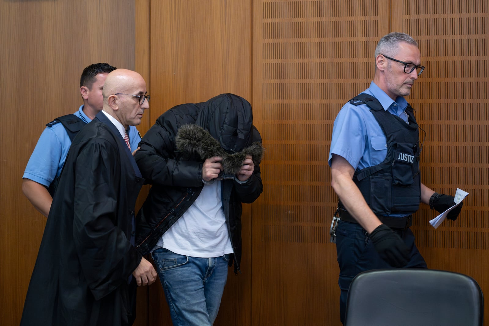 A Syrian doctor, center, accused of torture and war crimes in his Syrian homeland, is led into the courtroom next to his lawyer Oussama Al-Agi, 2nd left, for the verdict, in the Higher Regional Court in Frankfurt, Germany, Monday, June 16, 2025. (Boris Roessler/dpa via AP)