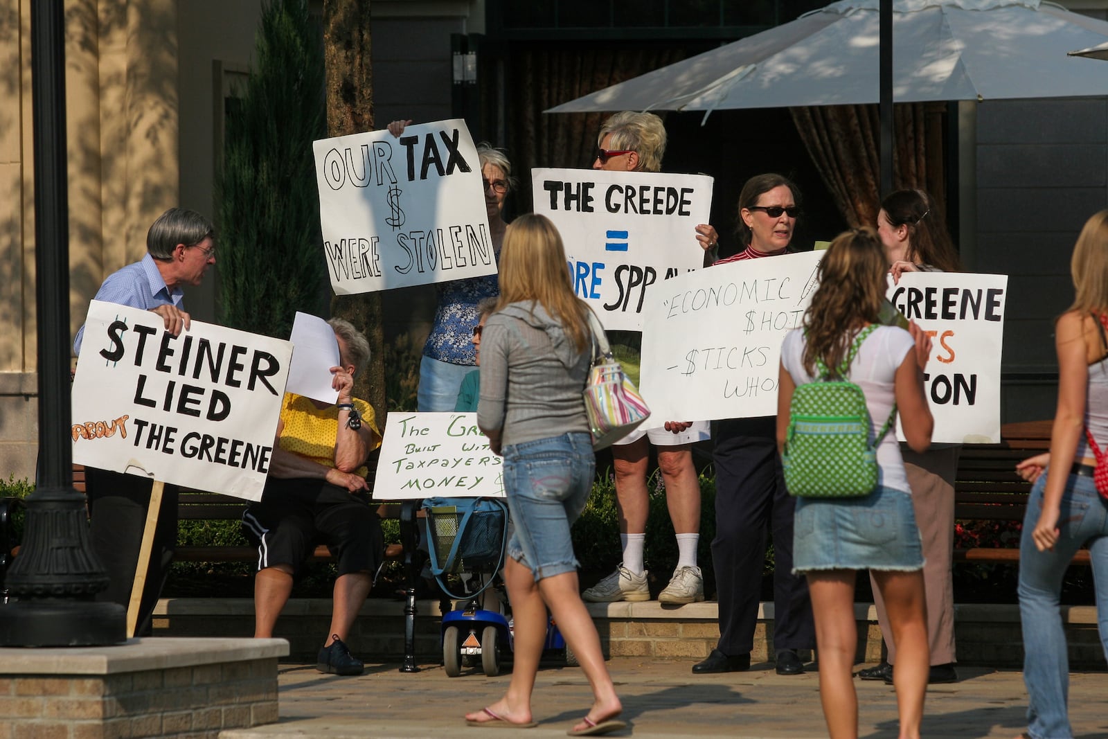 Protestors hold signs along the town square during Thursday's grand opening of The Greene in Beavercreek. PHoto by Lisa Powell