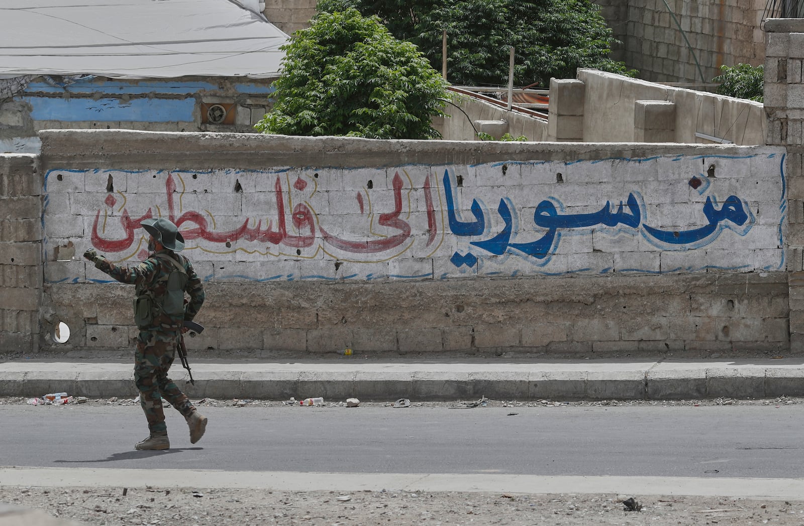 A Syrian government security forces gunman passes in front of an Arabic graffiti that reads "From Syria to Palestine", at one of Jaramana suburb entrances, after clashes erupted in the area between members of the minority Druze sect and pro-government fighters, in the southern suburb of Jaramana, Damascus, Syria, Wednesday, April 30, 2025. (AP Photo/Omar Sanadiki)