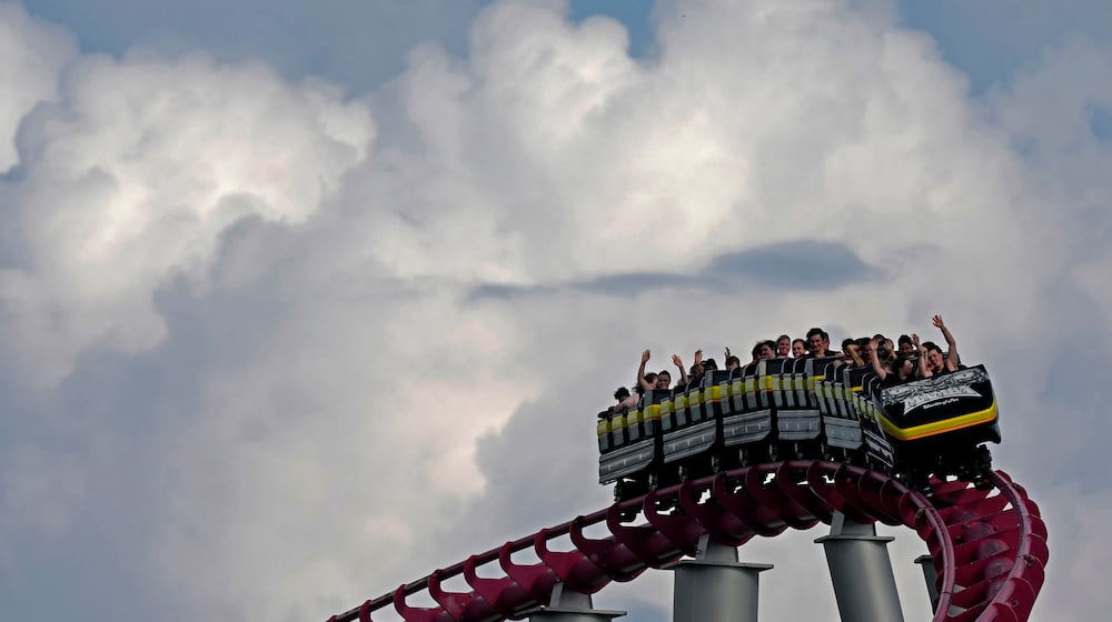 People ride on the Mamba roller coaster at Worlds of Fun theme park as storm clouds build in the distance on the first full day of summer Friday, June 21, 2024, in Kansas City, Mo. (AP Photo/Charlie Riedel)