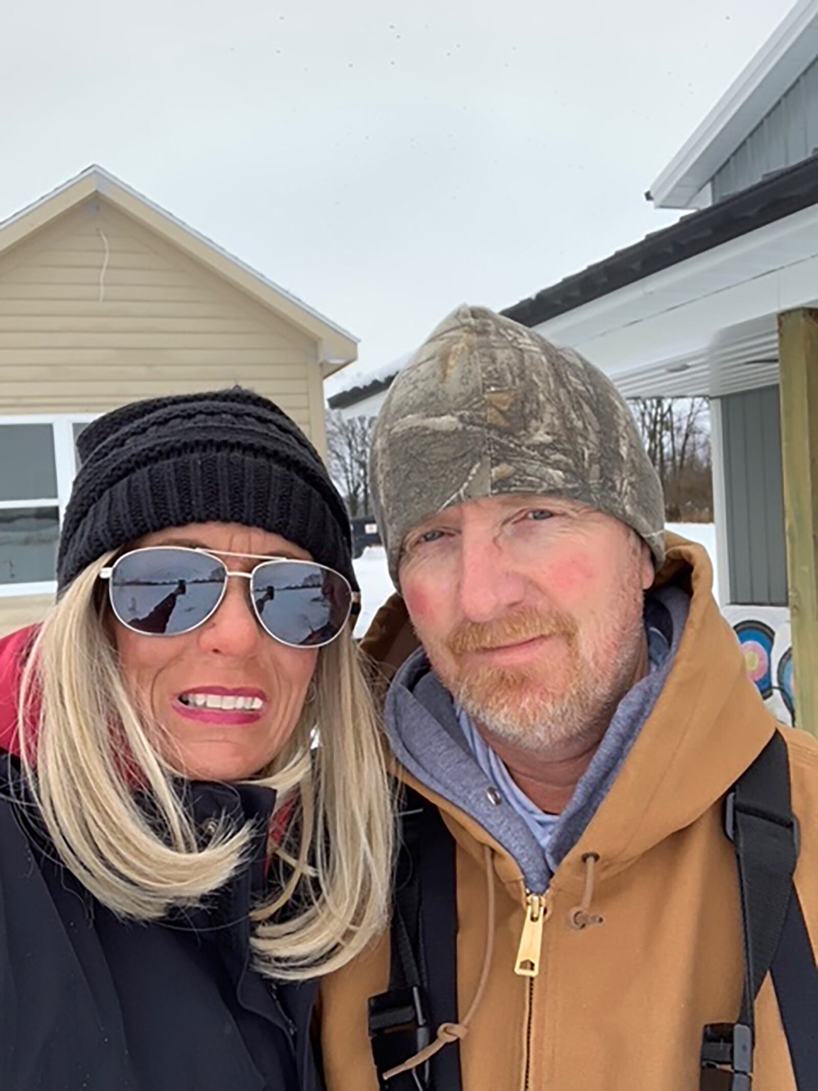 Carrie (L) and Matt Kendall at location of their new home in January of 2021. She had begun losing her hair and was wearing a "topper" and hat to cover the bare spots.