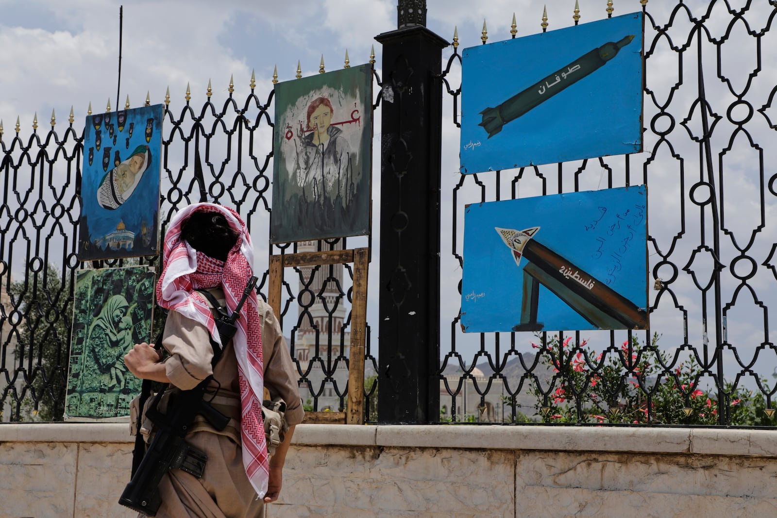 A Yemeni gunman walks past paintings depicting rockets and scenes in solidarity with Gaza, displayed on a roadside fence in Sanaa, Yemen, Monday, May 5, 2025. (AP Photo/Osamah Abdulrahman)